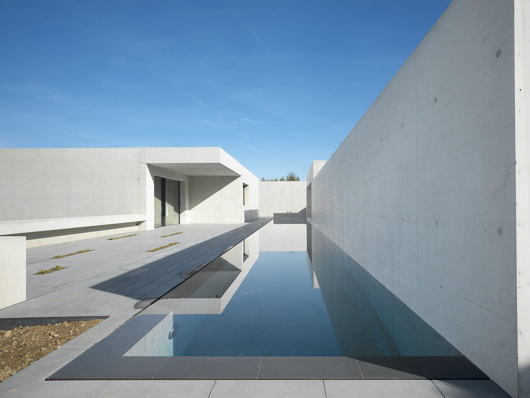 Minimalist concrete courtyard with a long reflecting pool under a clear sky