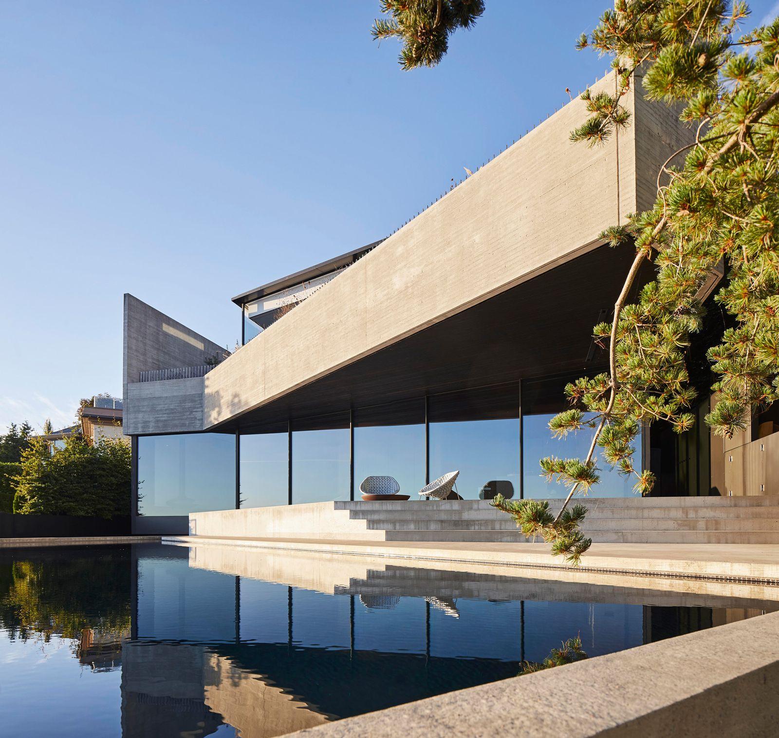 Modern concrete residence with a cantilevered roof reflected in a still pool