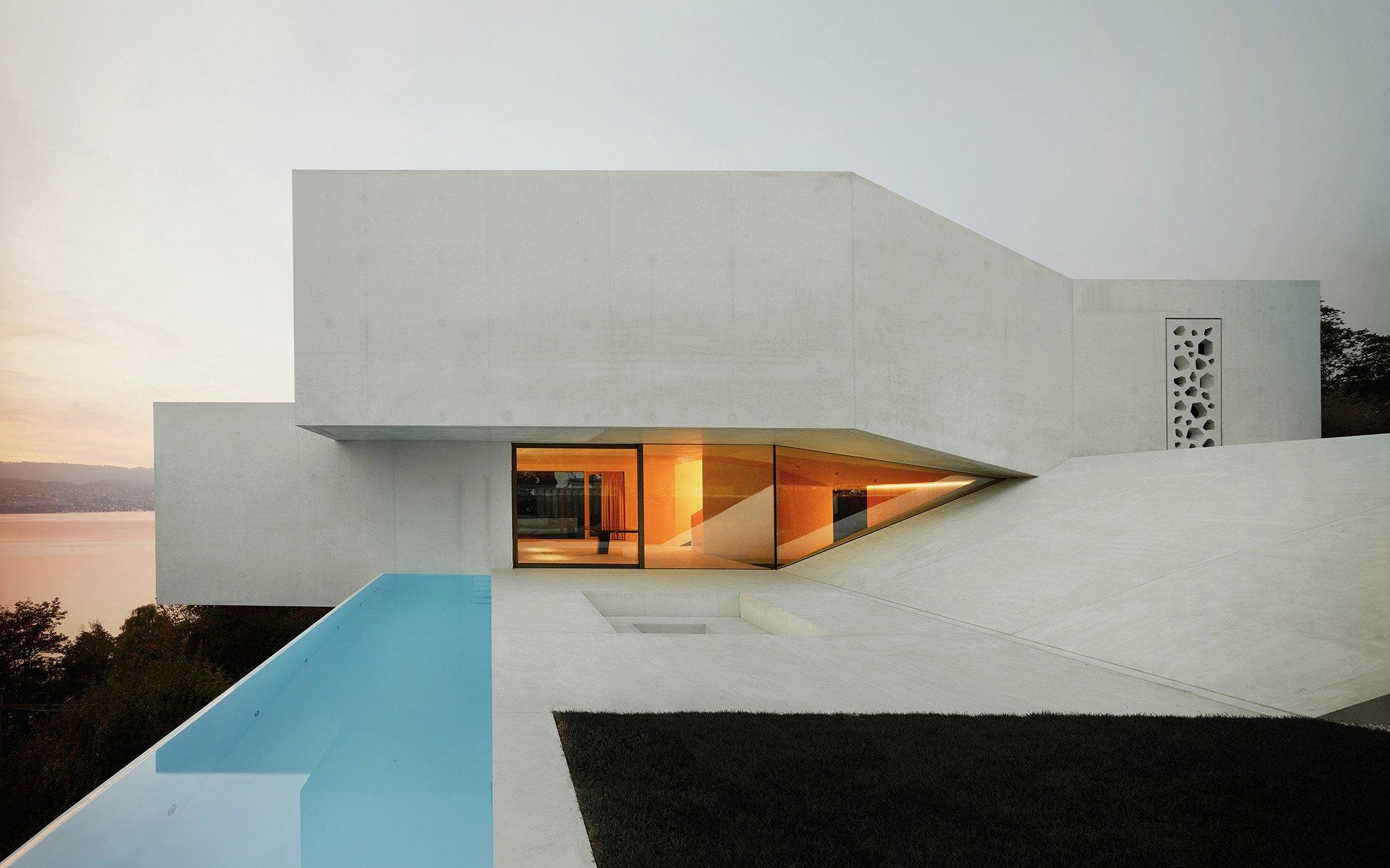 White geometric concrete residence with a blue pool at dusk
